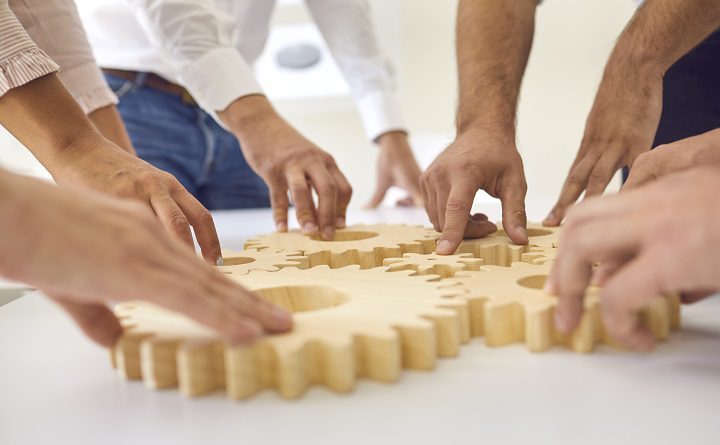 Teamwork, cooperation and successful development concept. Hands of business people making whole picture of wooden gears on table together in office