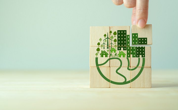 Eco friendly, green company culture concept. Carbon nautral and net zero target. Sustainable enviroment and business. Build green community. Hand holds wooden cubes with eco globe on grey background.