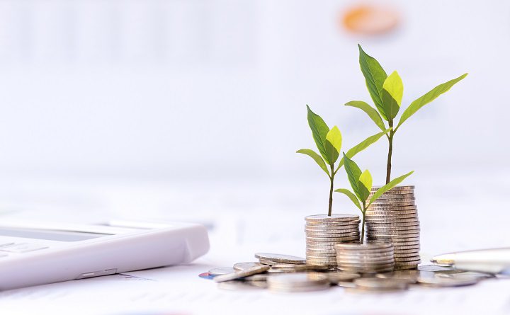 The tree  growing on money coin stack for investment,  business newspaper with financial report on desk of investor real estate business, city background.  Investment property growth Concept